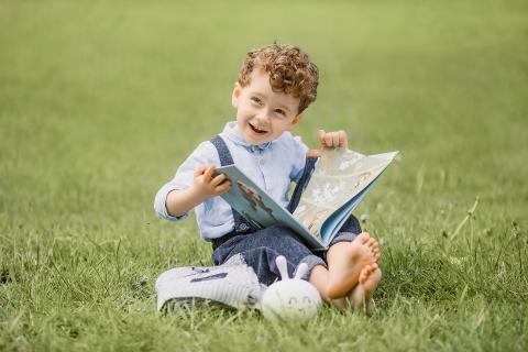 little boy reading a book outside