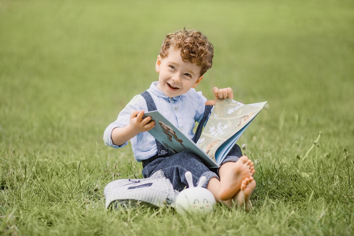 little boy reading a book outside